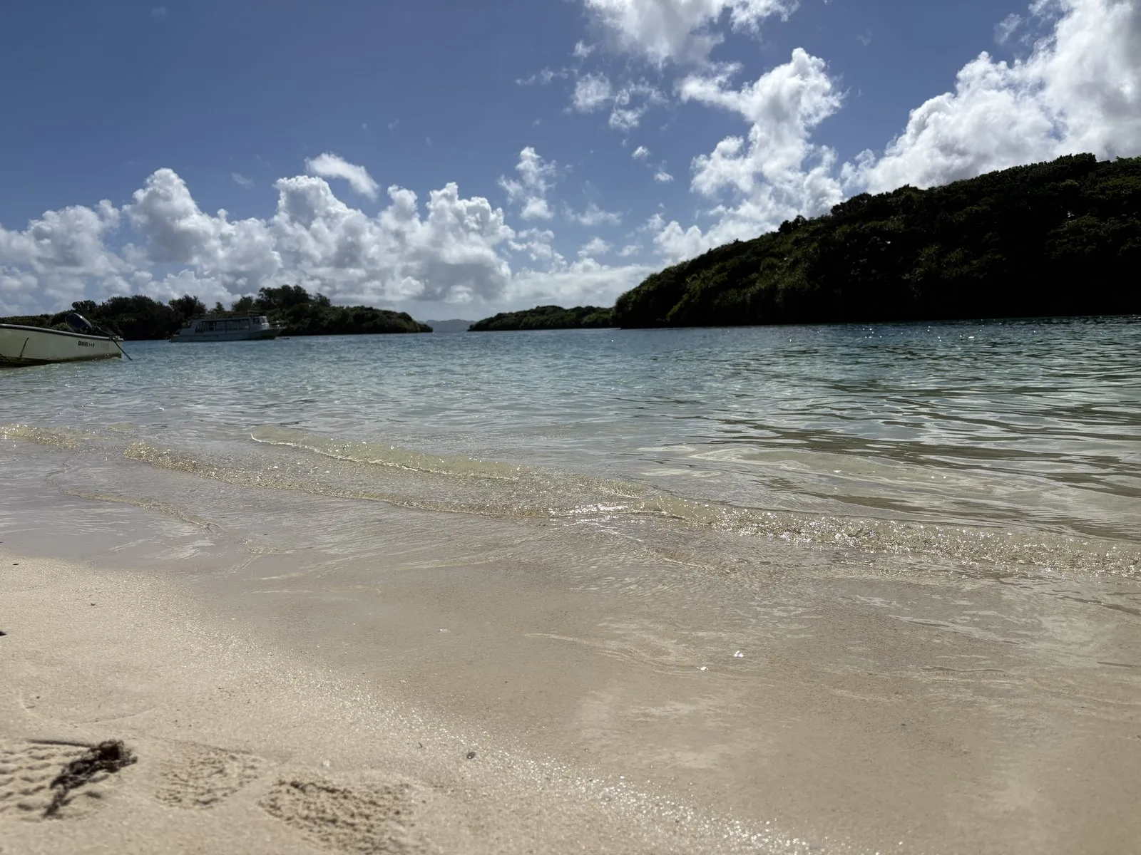 川平湾の波打ち際。白い砂と透き通った水の向こうに緑の小島とボートが浮かぶ