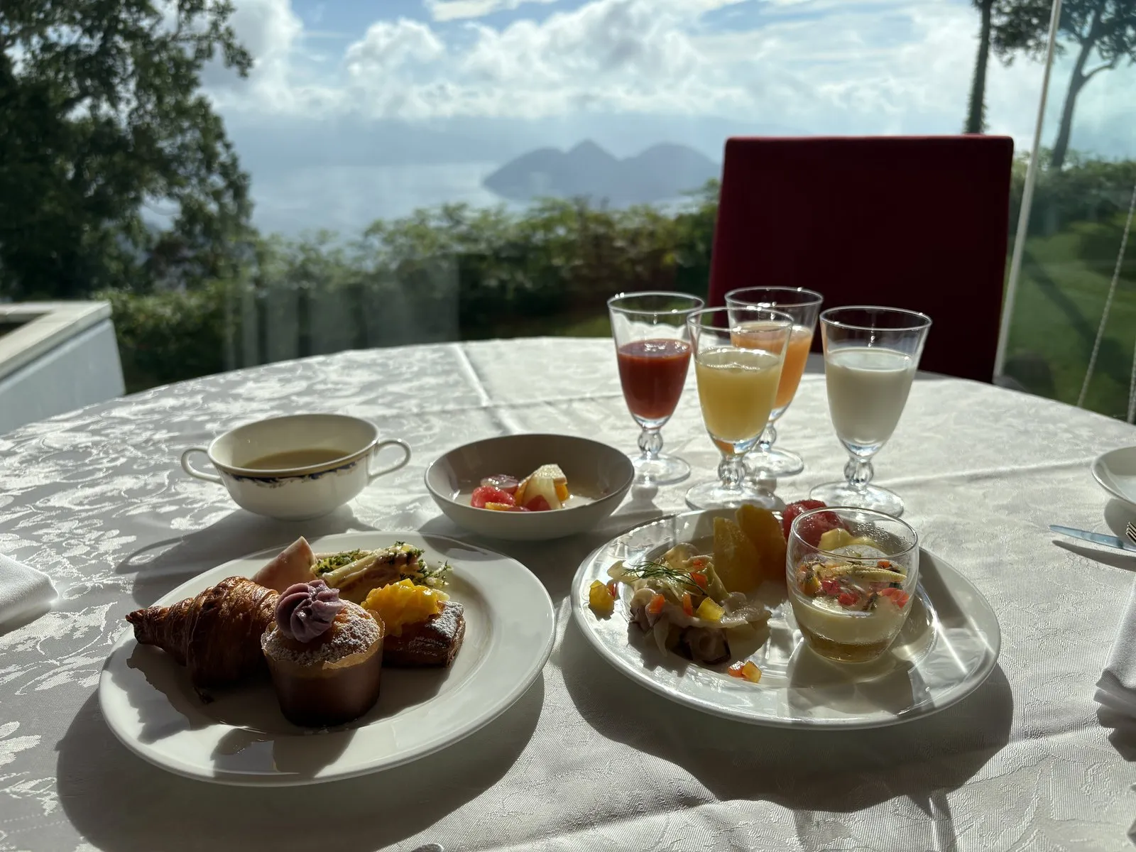 ザ・ウィンザーホテル洞爺の朝食。窓の外に洞爺湖と中島を望む席に、焼きたてのパンや前菜、ジュースが並ぶ